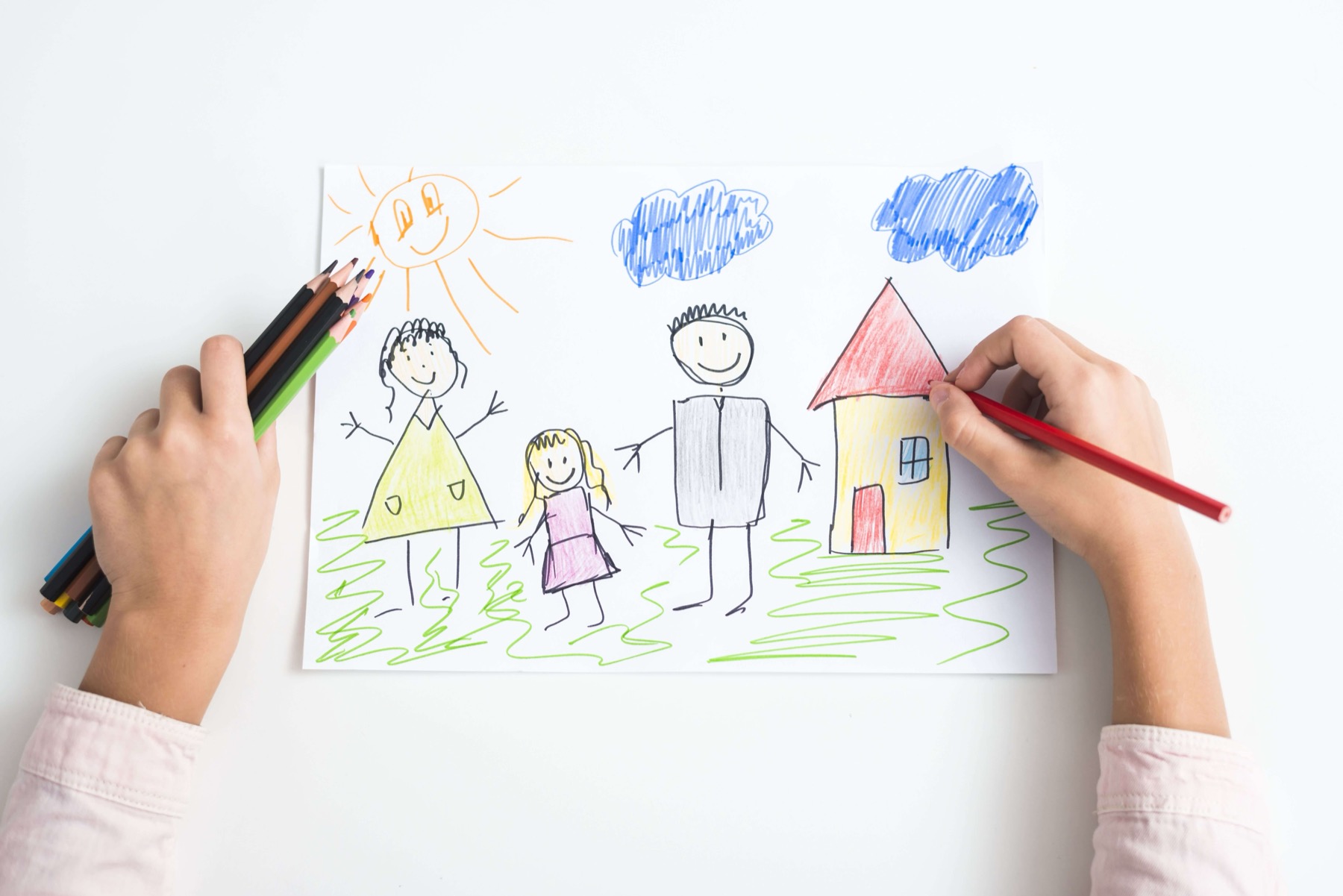 Child drawing a family and a house with colored pencils